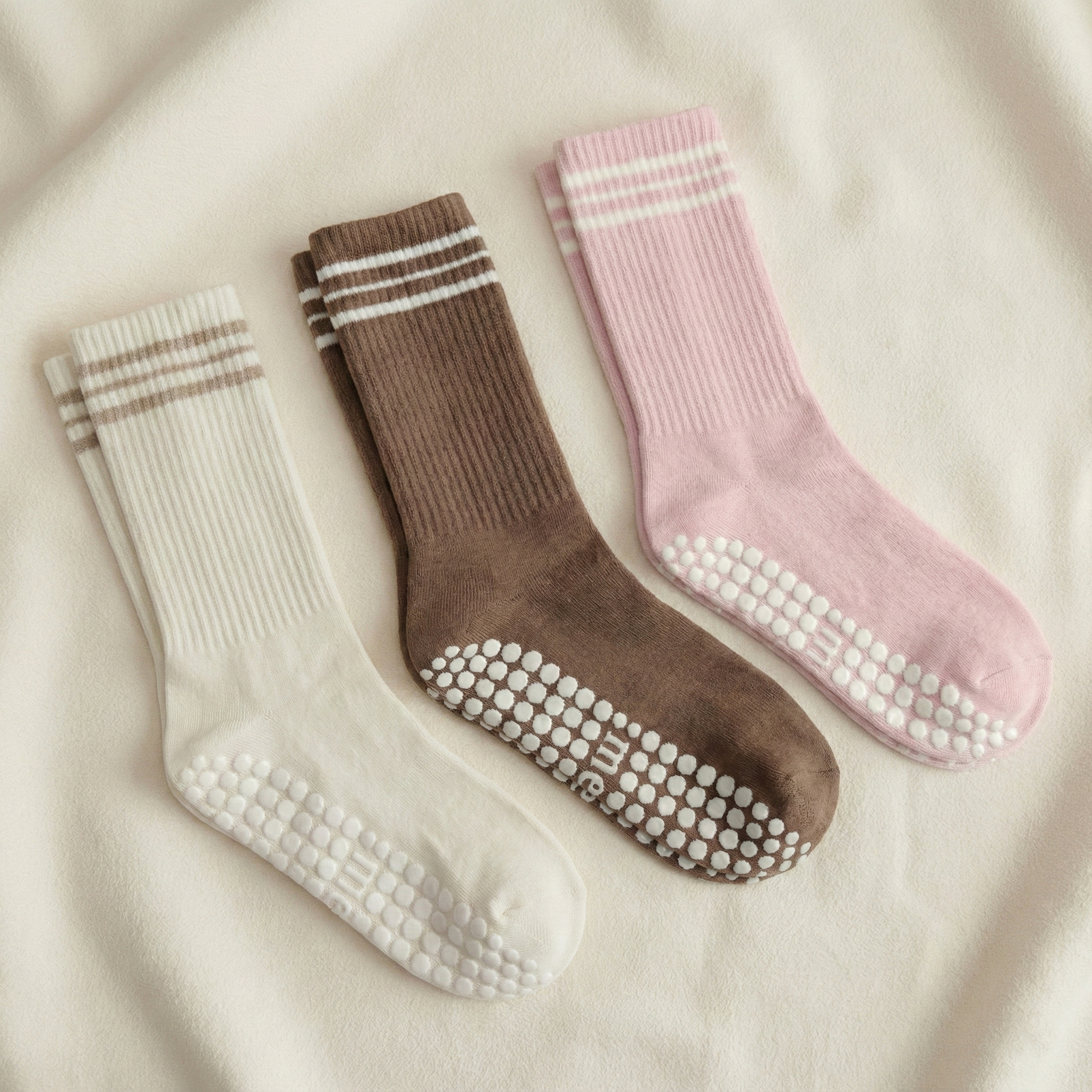 Three pairs of merino wool pilates grip socks in beige, brown, and pink on a beige background